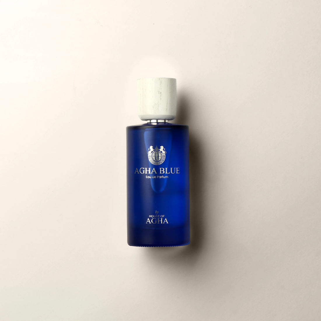 A bottle of Agha Blue Eau de Parfum by House of Agha, featuring a deep blue glass bottle with a white cap and elegant silver branding, placed against a plain background.