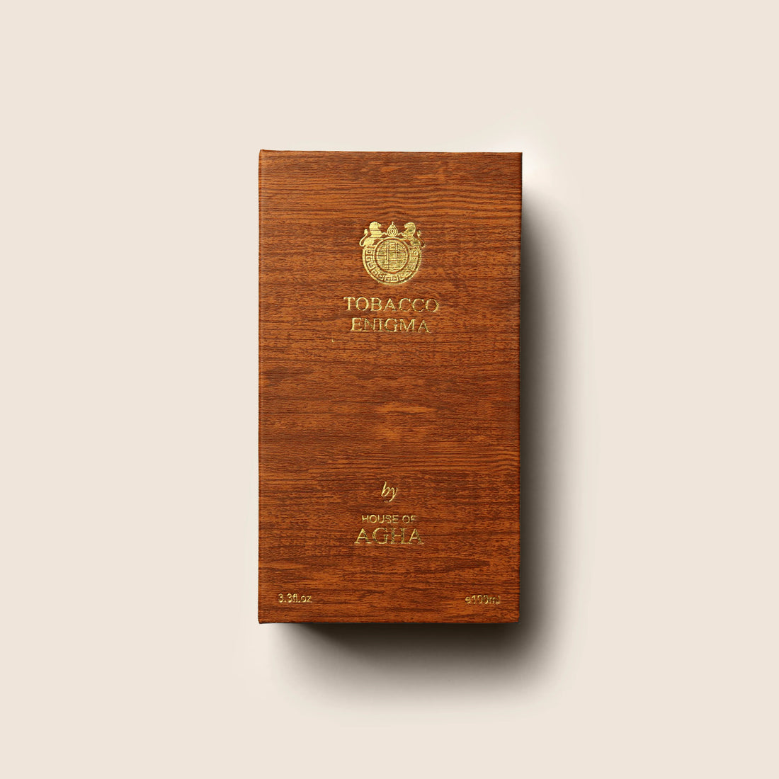 A bottle of Tobacco Enigma Eau de Parfum by House of Agha, featuring a light green glass bottle with a wooden cap and elegant gold branding, placed against a plain background.